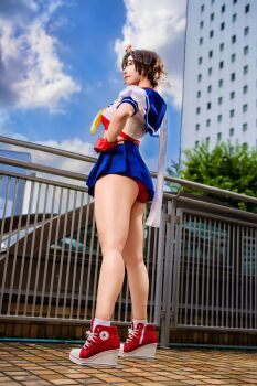  1girl asian ass blue_skirt brown_hair buruma cosplay cosplay_photo from_below hand_on_own_hip headband highres kasugano_sakura legs miniskirt photo_(medium) pleated_skirt puffy_short_sleeves puffy_sleeves purin_cosplay real_life red_buruma sailor_collar school_uniform serafuku shoes short_hair short_sleeves skirt sneakers socks street_fighter street_fighter_zero_(series) upskirt white_headband white_socks 