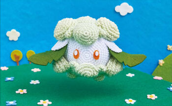 amigurumi_(medium) asako_ito commentary cottonee creature day english_commentary full_body gen_5_pokemon nintendo no_humans official_art outdoors photo_(medium) pokemon pokemon_(creature) pokemon_tcg solo third-party_source unconventional_media