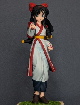 1girl ainu_clothes black_eyes black_hair breasts doll fingerless_gloves gloves highres index_finger_raised legs long_hair medium_breasts nakoruru open_mouth photo_(medium) pointing pointing_at_viewer real_life samurai_spirits smile snk solo the_king_of_fighters thighs tongue weapon