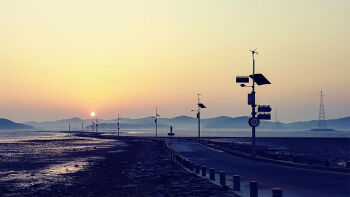 commentary_request evening hoshiumisora lamppost landscape mountainous_horizon no_humans original outdoors photorealistic realistic road road_sign scenery sign sky sun sunset transmission_tower yellow_sky