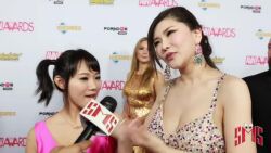 2girls animated asian audible_speech black_hair breasts brown_eyes cleavage dress earrings english_audio huge_breasts indoors interview japanese_(nationality) jewelry kiss long_dress matching_hair/eyes microphone multiple_girls necklace okita_anri photo_(medium) real_life shibuya_kaho size_difference sound standing tagme video yuri