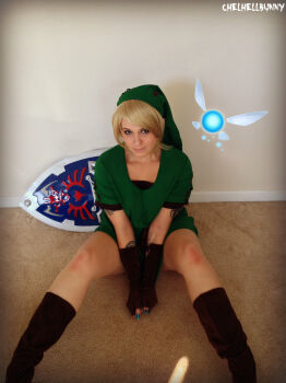 Rule 34 | 1girl, blonde hair, boots, chelhellbunny, cosplay, female focus, gloves, highres, hood, linkle, linkle (cosplay), looking at viewer, nail polish, nintendo, photo (medium), real life, shield, sitting, smile, solo, the legend of zelda