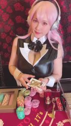 1girl animated breasts card card_(medium) cleavage cleavage_cutout clothing_cutout cosplay female_focus headphones highres holding holding_card japanese_(nationality) large_breasts long_hair looking_at_viewer model nitroplus photo_(medium) pink_eyes pink_hair poker real_life shibuya_kaho smile solo sound super_sonico super_sonico_(cosplay) video