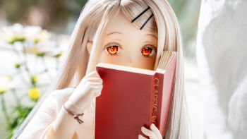 1girl blonde_hair book character_doll day doll doll_joints figure_(medium) gakuen_idolmaster hair_ornament hairclip highres holding holding_book idolmaster joints long_hair looking_at_viewer orange_eyes photo_(medium) red_eyes shinosawa_hiro solo unconventional_media