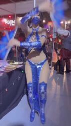 1girl 6+others animated arms_up black_hair cosplay curvy face_mask hand_fan highres kitana looking_at_viewer mask mortal_kombat_(2011) mortal_kombat_(series) mouth_mask multiple_others navel ninja photo_(medium) ponytail real_life solo sophie_valentine standing video wide_hips