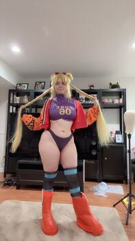 Rule 34 | 1girl, blonde hair, breasts, cosplay, curvy, double bun, gloves, green eyes, hair bun, indoors, jacket, lips, long hair, long twintails, medium breasts, musclemommycosplay, navel, one piece, open clothes, open jacket, orange jacket, photo (medium), real life, revealing clothes, single glove, smile, thong, vegapunk york, vegapunk york (cosplay), wide hips
