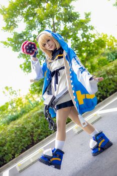 1boy 2024 absurdres androgyne_symbol androgynous aqua_eyes arc_system_works asian black_skirt blonde_hair blue_shoes blurry blurry_background blush brand_name_imitation bridget_(guilty_gear) bridget_(guilty_gear)_(cosplay) bush chain commentary cosplay cosplay_photo cross cuffs day depth_of_field dutch_angle fingerless_gloves full_body gloves green_eyes grey_background grin guilty_gear guilty_gear_strive habit handcuffs highres holding holding_weapon hood hood_up hoodie jacket japanese_(nationality) lips lipstick long_sleeves looking_at_viewer makeup male_focus medium_hair miniskirt one_eye_closed open_clothes open_hoodie outdoors photo_(medium) pleated_skirt pointing pointing_at_viewer puffy_long_sleeves puffy_sleeves real_life shadow shoes skirt smile socks solo spread_fingers standing standing_on_one_leg teeth trap tree turtleneck upper_teeth_only walking weapon wink yo-yo yunomi_ochawan