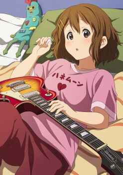 1girl :o absurdres brown_eyes brown_hair collarbone doll electric_guitar gibson_les_paul guitar hair_ornament hairclip head_on_pillow heart heart_print highres hirasawa_yui holding holding_plectrum instrument k-on! lying on_back on_bed pants parted_lips pillow pink_shirt plectrum print_shirt red_pants shirt short_hair solo sumaboooo t-shirt