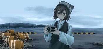 1girl beanie black_eyes black_hair camera closed_mouth collared_shirt earflap_beanie hat highres holding holding_camera long_sleeves ocean original outdoors overcast pale_skin shirt sky solo sweater_vest upper_body yoshiryuu