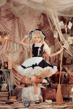 1girl absurdres apron blonde_hair book book_stack braid broom carpet cosplay cosplay_photo couch full_body hand_on_headwear hat highres holding holding_broom indoors kirisame_marisa lamp light_smile long_hair looking_at_viewer mini-hakkero photo_(medium) pillow shirt shoes side_braid sinkai_cos solo standing standing_on_one_leg touhou waist_apron white_apron white_shirt white_wrist_cuffs wrist_cuffs