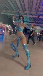 1girl 6+others animated arms_up black_hair cosplay face_mask hand_fan highres kitana looking_at_viewer mask mortal_kombat_(2011) mortal_kombat_(series) mouth_mask multiple_others navel ninja photo_(medium) real_life solo sophie_valentine standing thong video walking wide_hips